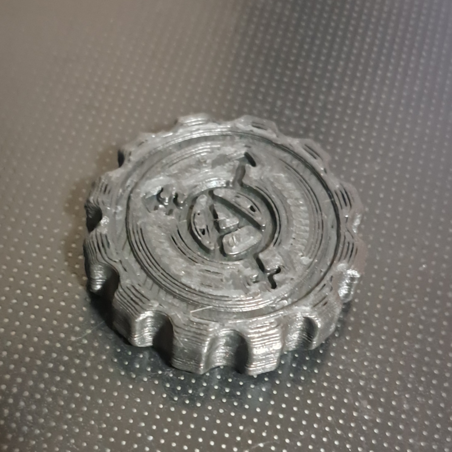 The top of Silver's maker coin, displaying a trans anarchy symbol recessed a millimeter into the material.